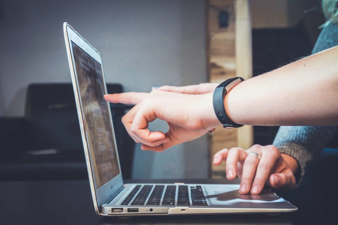 A laptop with one pair of hands using the mousepad while another points at the screen while looking at a Google Analytics report.