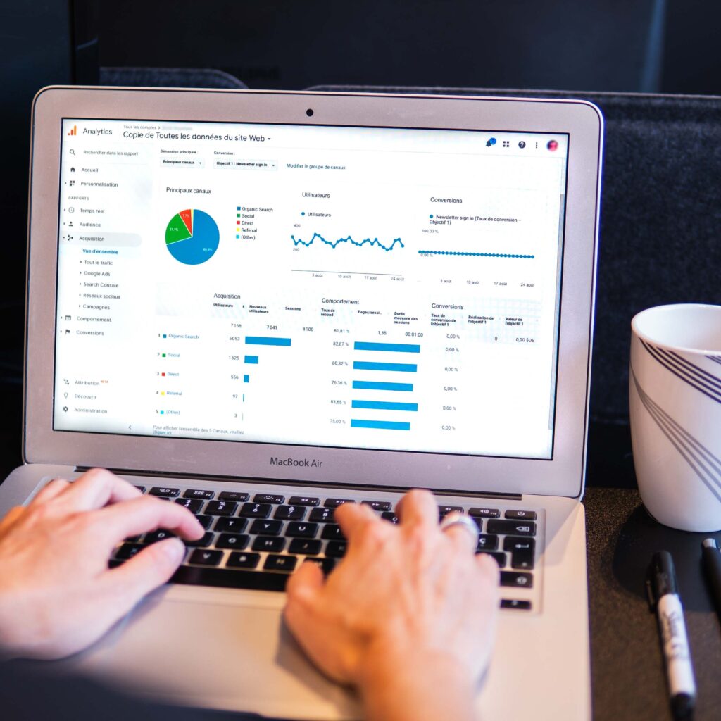 A pair of hands types an a Mac laptop computer while examining a Google Analytics report to prepare for the switch from Universal Analytics to GA4.