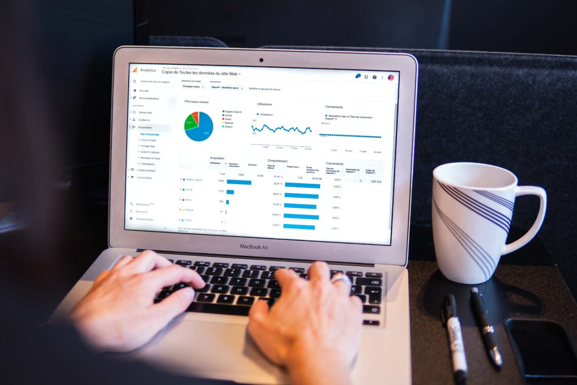 A pair of hands types an a Mac laptop computer while examining a Google Analytics report to prepare for the switch from Universal Analytics to GA4.