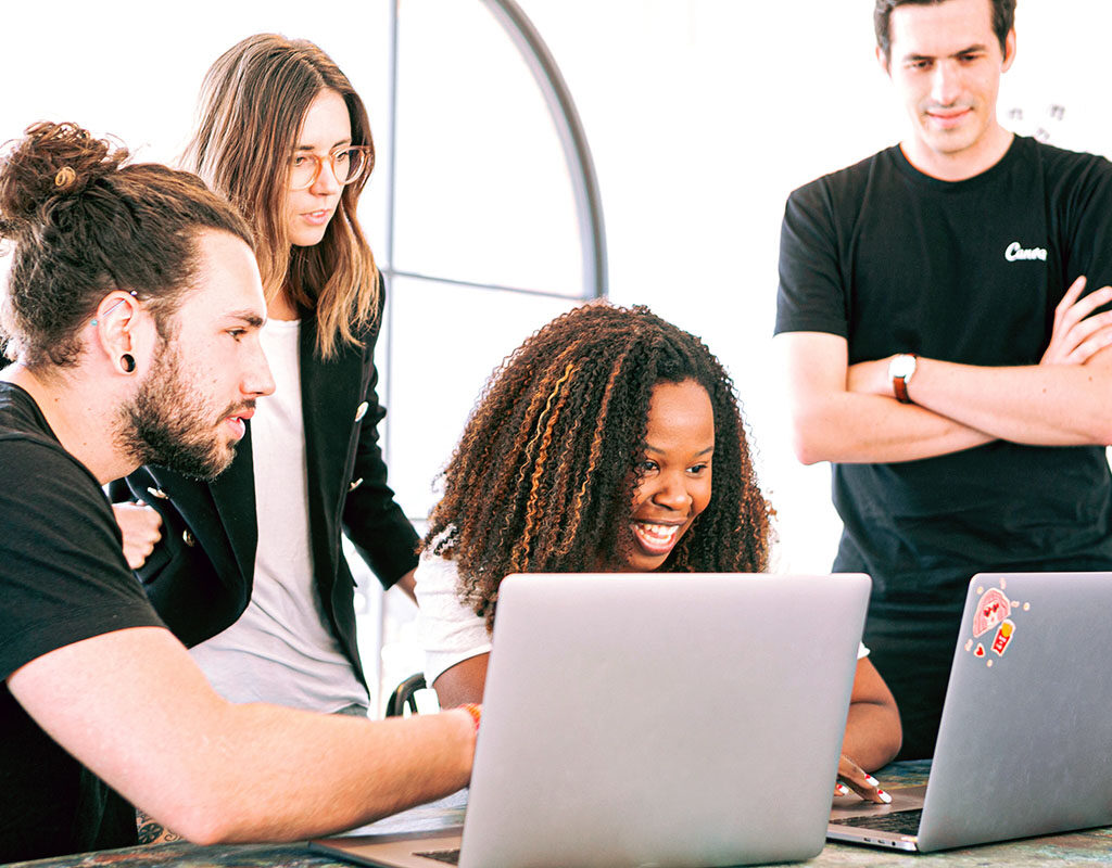 Four people sit and stand around two laptops as they study SEO and digital marketing for their online business.